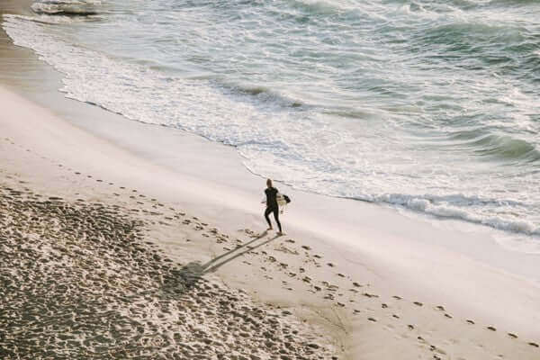 Person walking on a sandy beach near ocean waves, leaving footprints in the sand, symbolizing embracing one's convictions and journey.