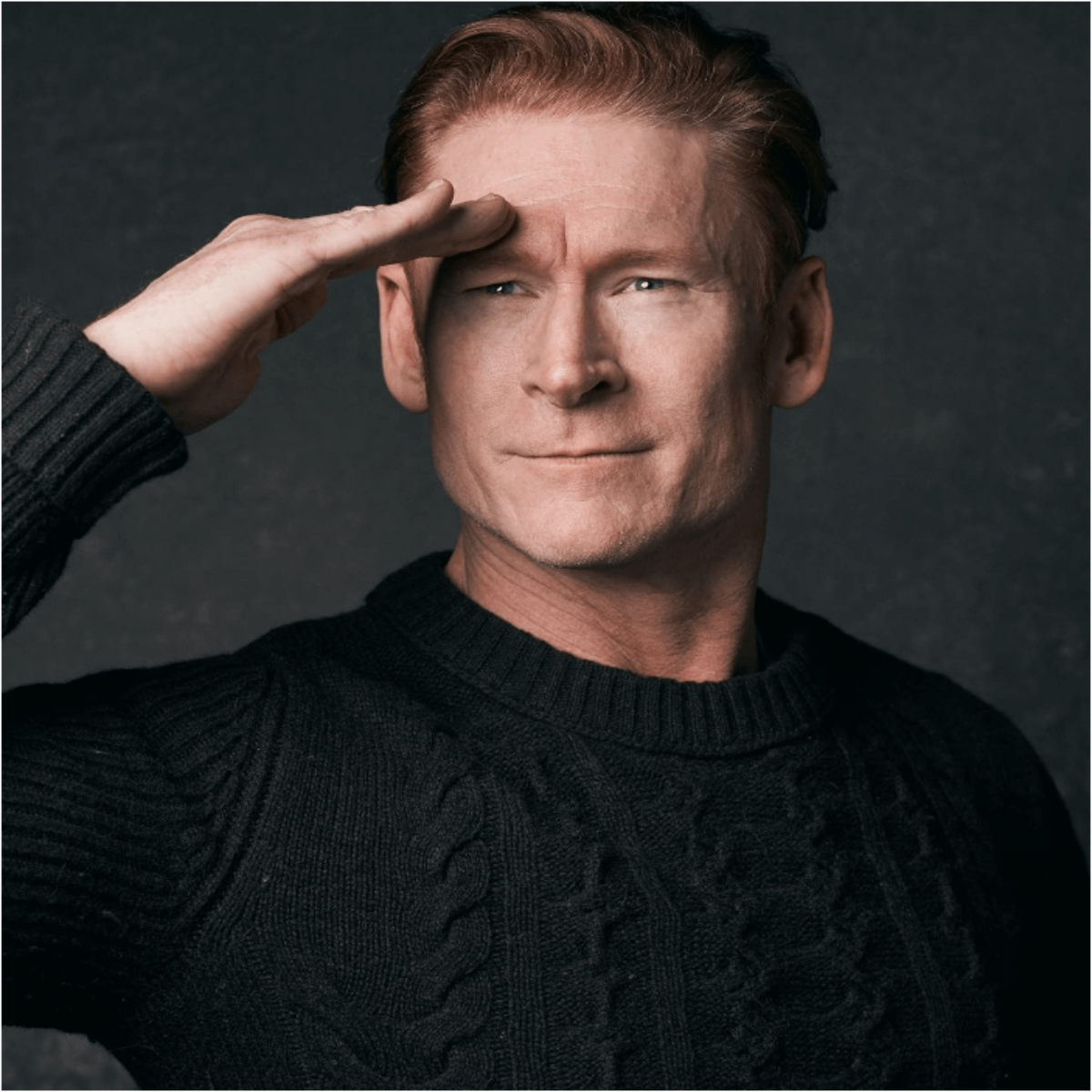 Person saluting confidently in a dark sweater, against a neutral background.
