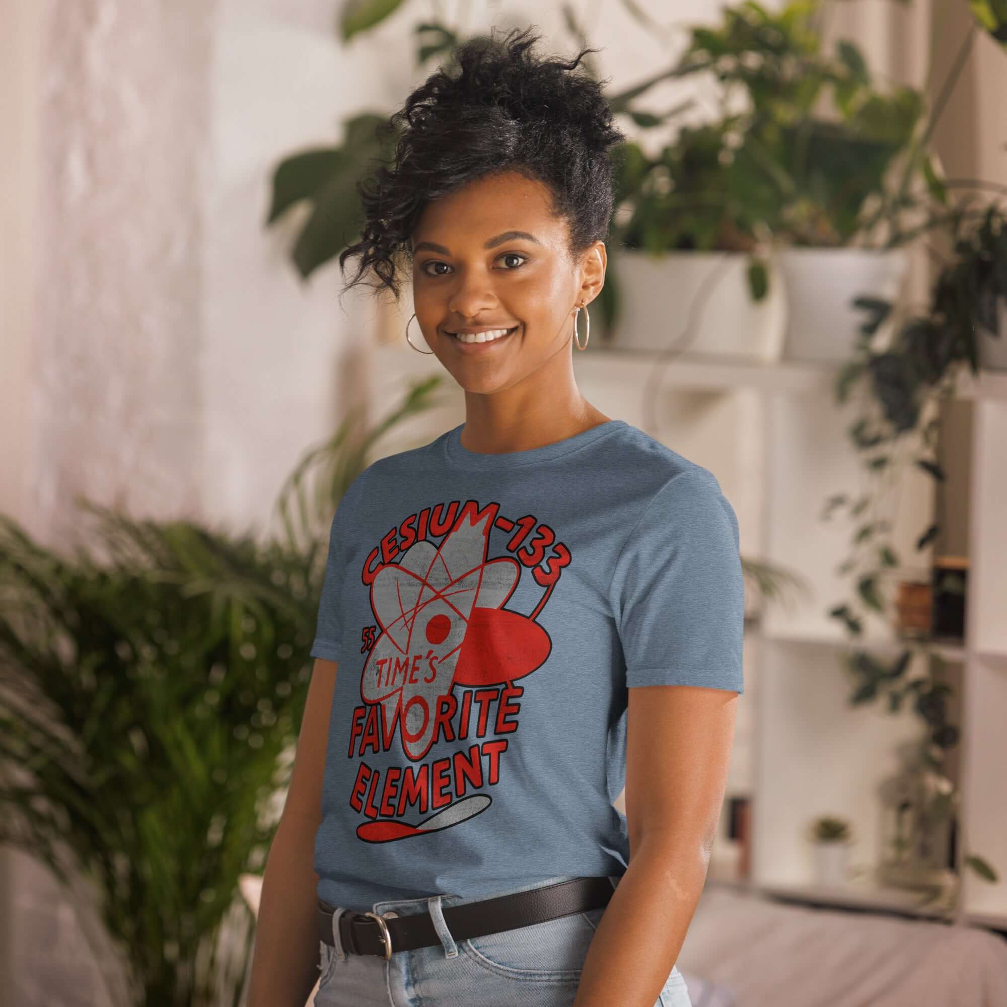 Woman wearing Cesium-133 Atomic Clock T-Shirt in blue with "Time's Favorite Element" design, smiling indoors.