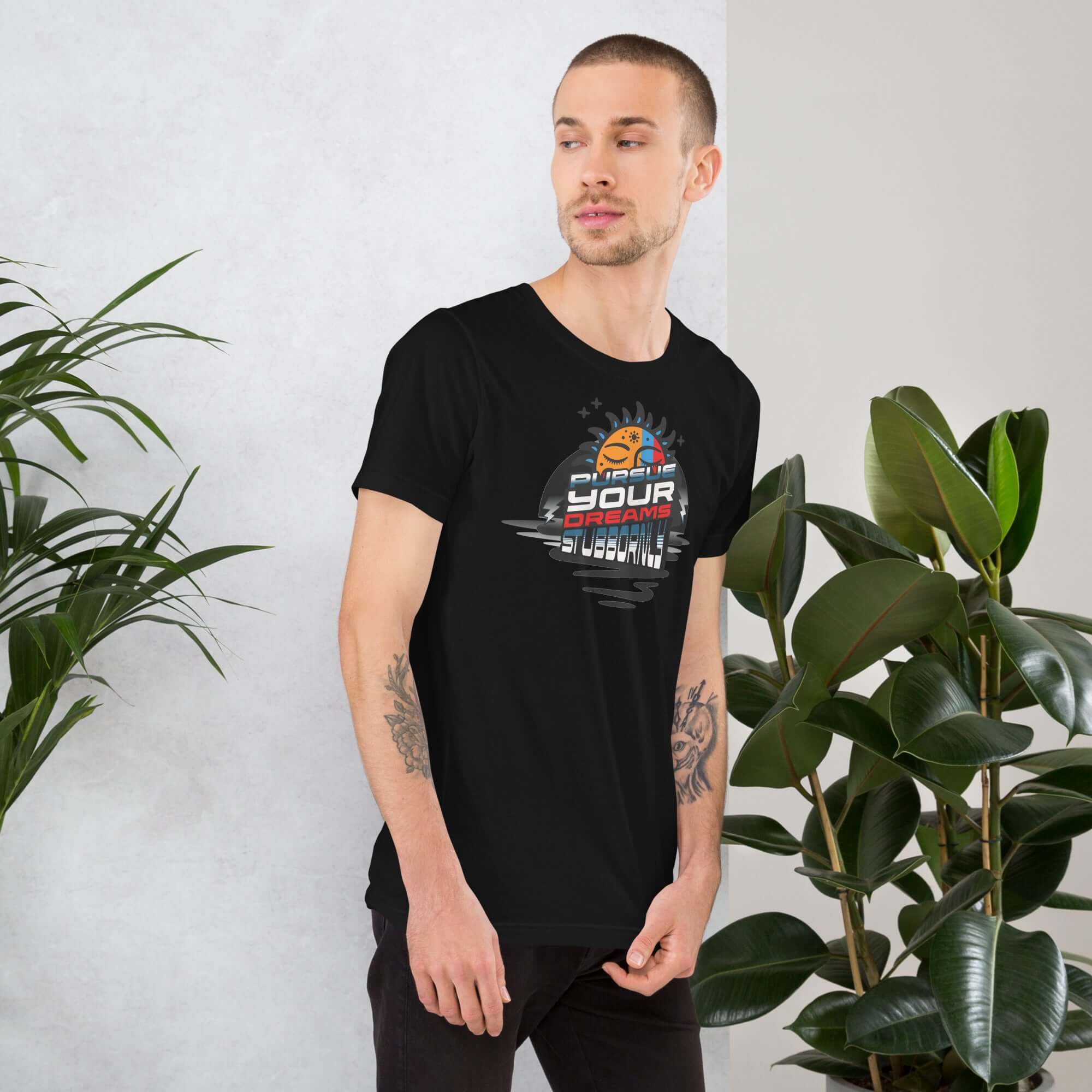 Man wearing Pursue Your Dreams Stubbornly T-shirt by Cosmic Motivation Apparel next to houseplants, promoting determination and cosmic style.