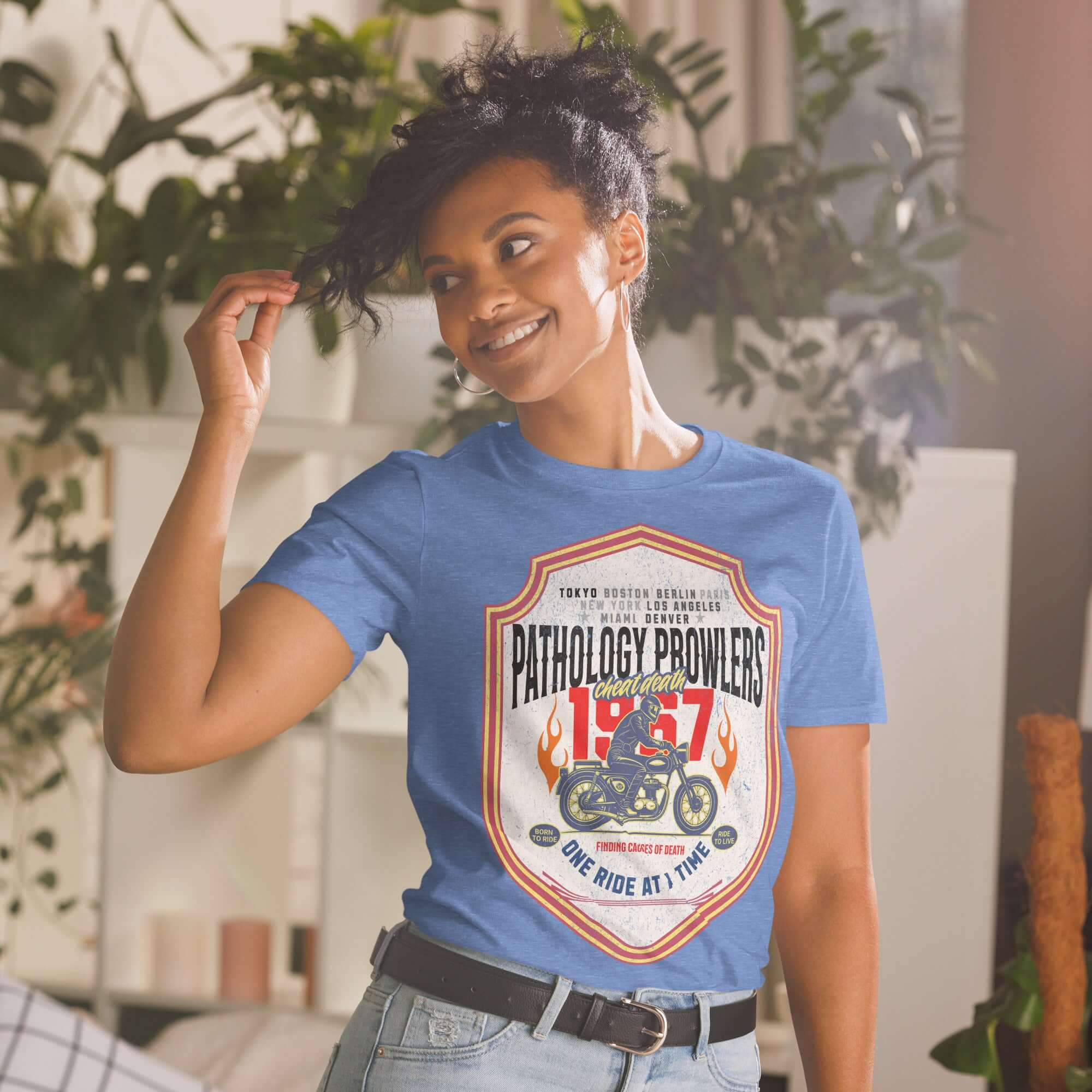 Woman wearing Pathology Prowlers MC T-Shirt with shield emblem, celebrating forensic motorcycle club, founded in 1967.