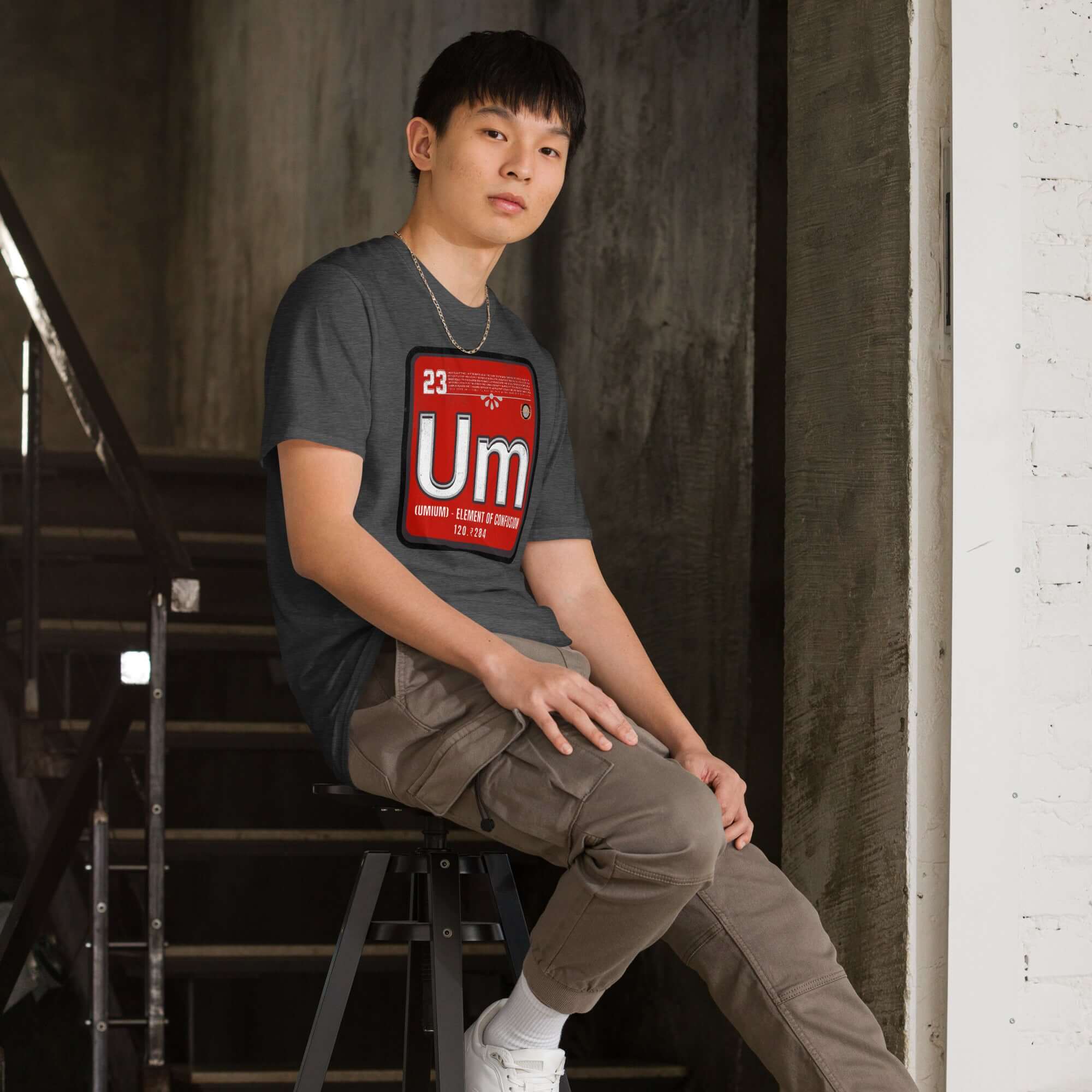 Person wearing Umium Element T-Shirt, Periodic Table of Confusion design, sitting on stairs with a vibrant red element symbol.